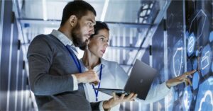 A gentleman and a lady carrying a laptop and looking at a server